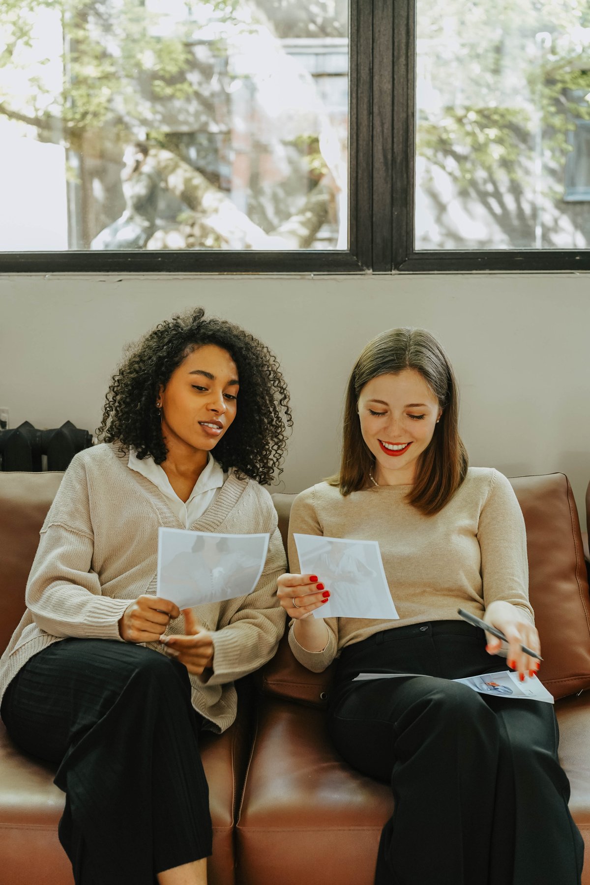 A Pair of Women Sitting on Couch Holding Papers